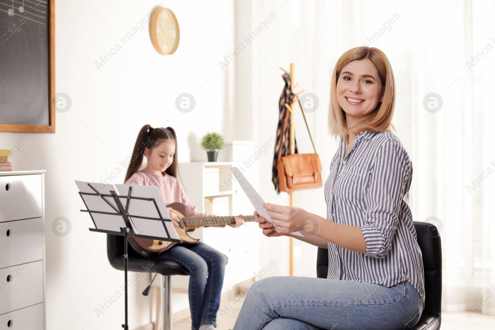 Photo of Little girl playing guitar with her teacher at music lesson. Learning notes