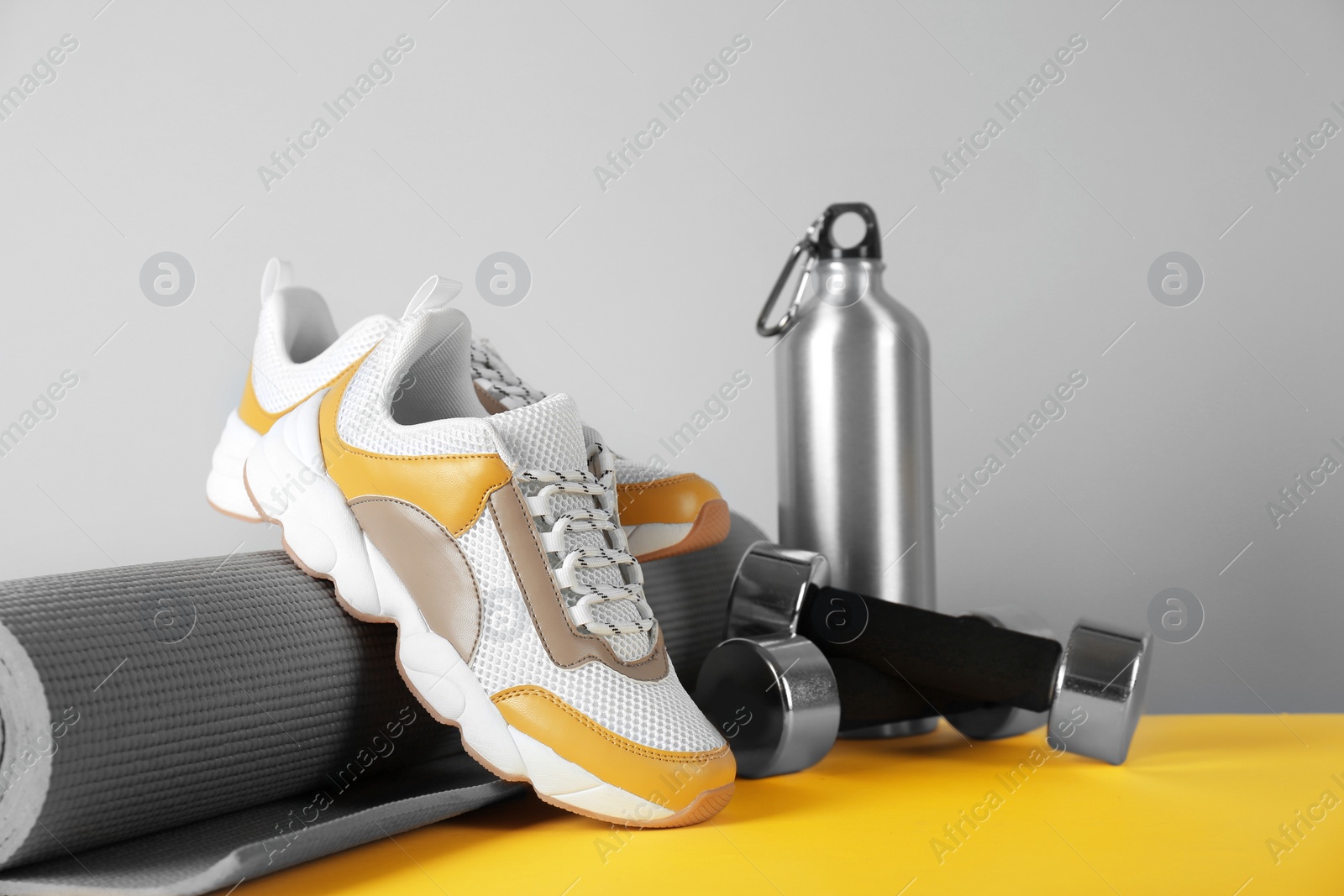 Photo of Composition of modern training shoes with mat, bottle and dumbbells on table