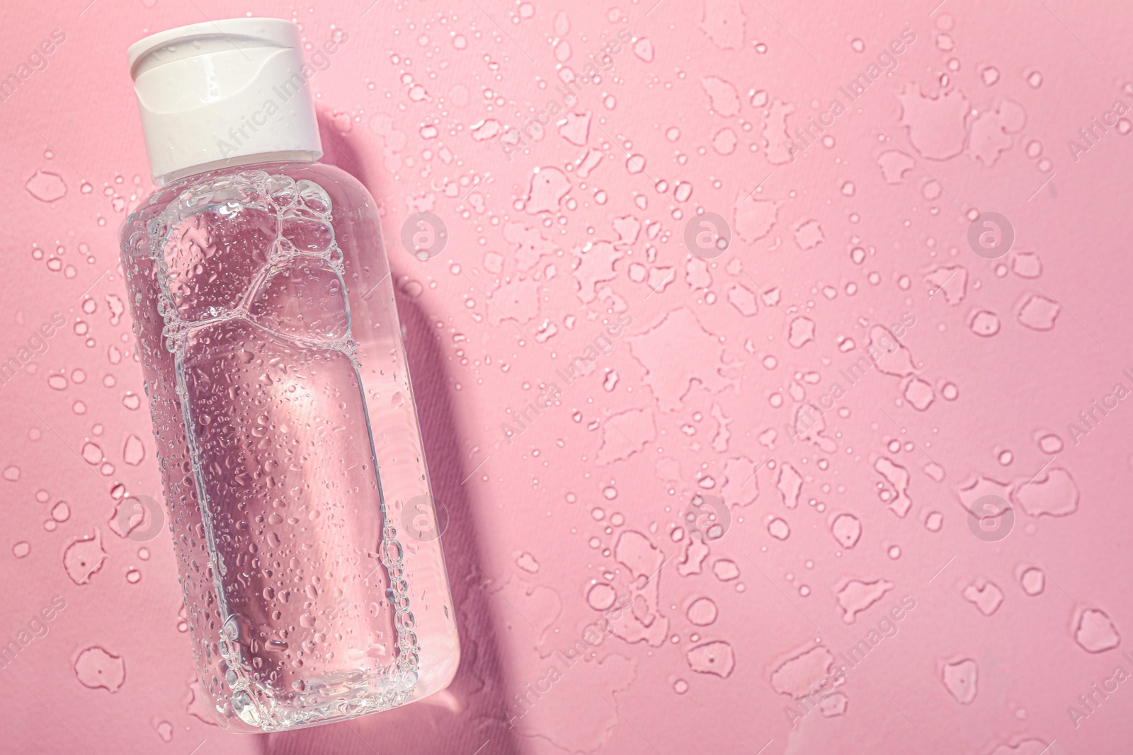 Photo of Wet bottle of micellar water on pink background, top view. Space for text