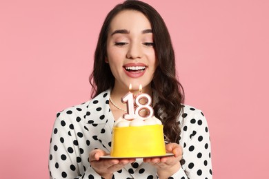 Photo of Coming of age party - 18th birthday. Smiling woman holding delicious cake with number shaped candles on pink background