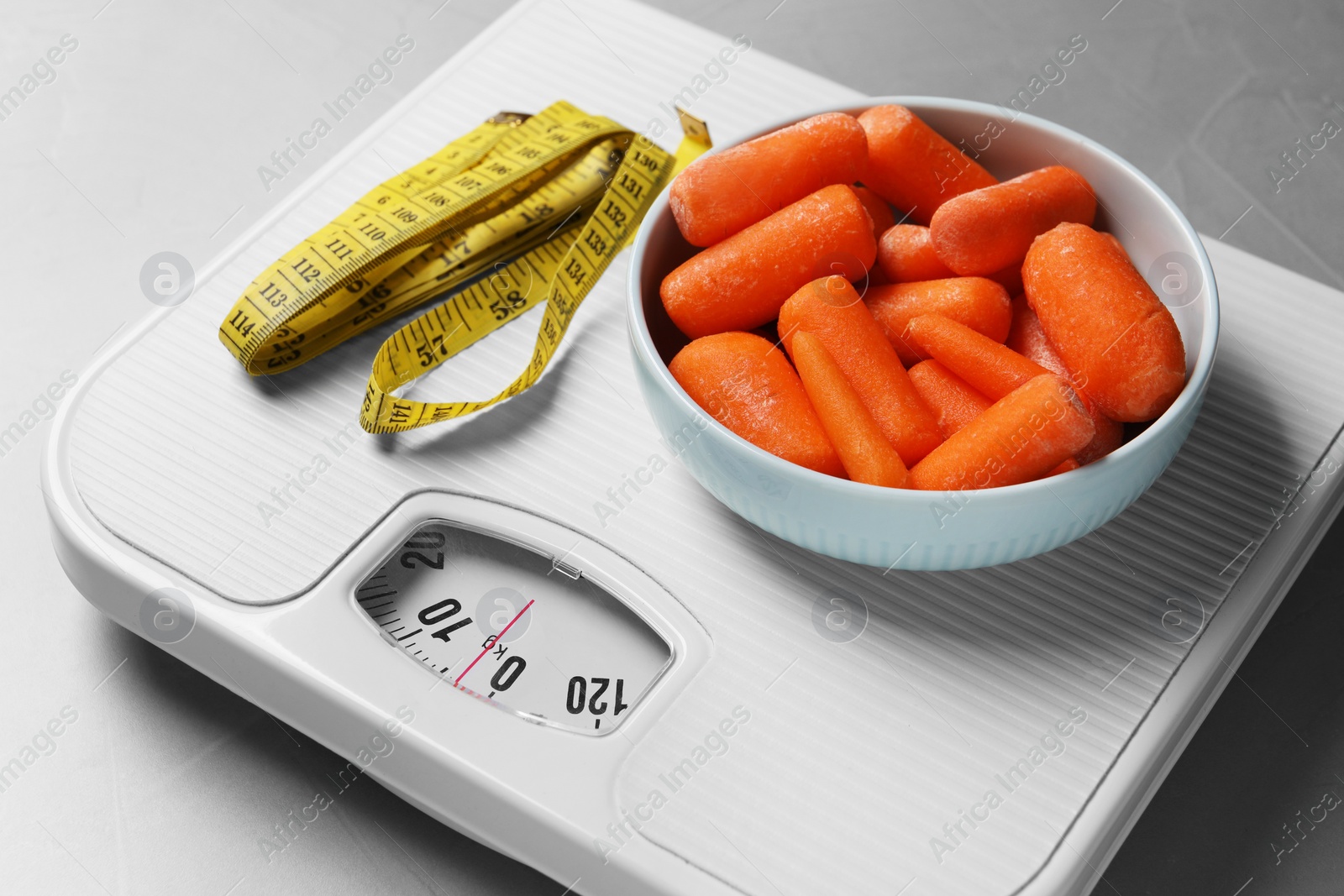 Photo of Healthy diet. Scale with carrots and measuring tape on light grey table, closeup