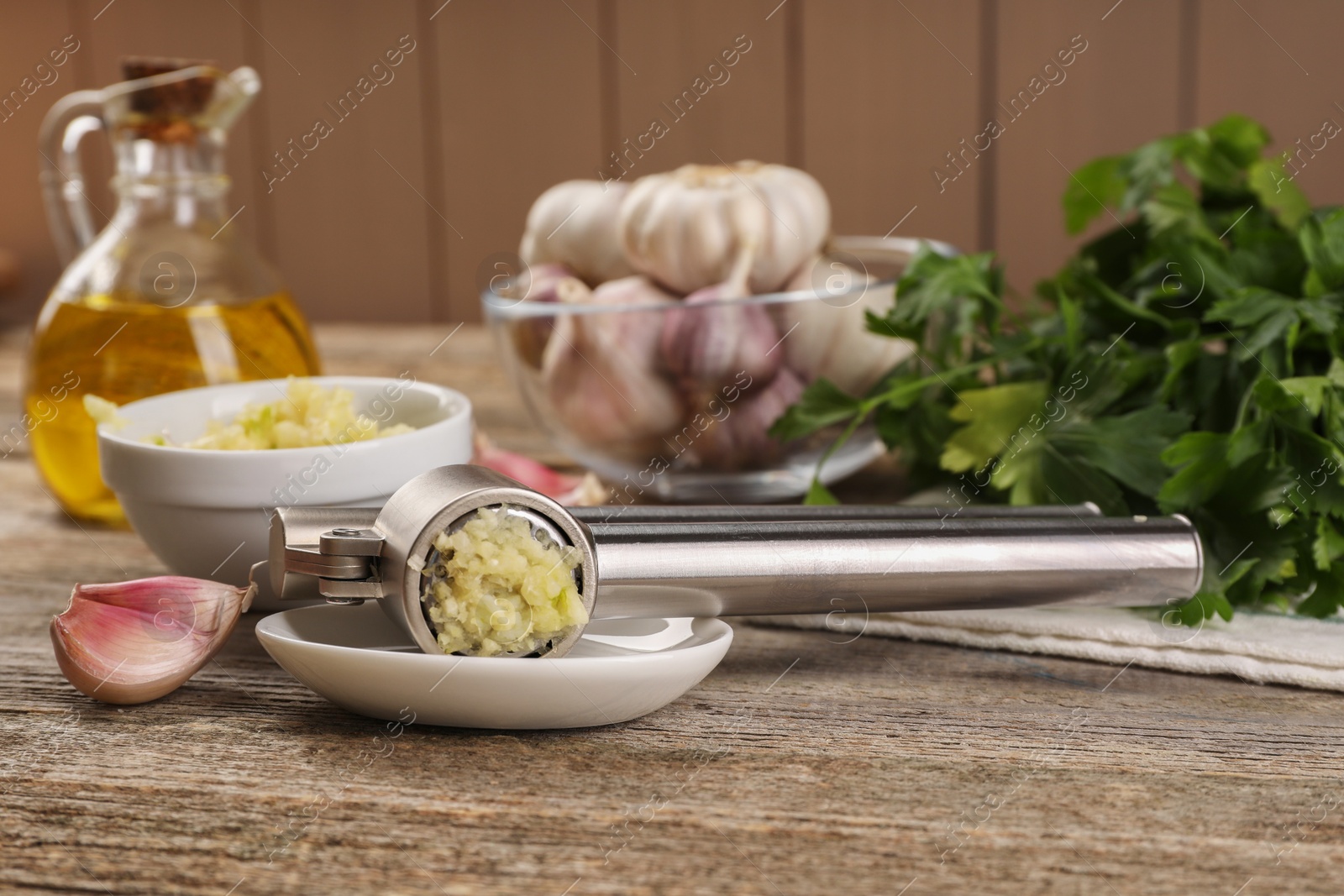 Photo of Garlic press with mince and cloves on wooden table, closeup