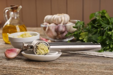 Garlic press with mince and cloves on wooden table, closeup