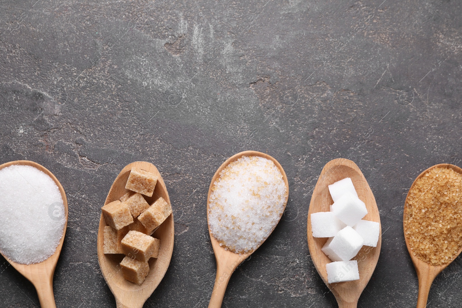 Photo of Spoons with different types of sugar on gray textured table, flat lay. Space for text