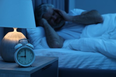 Photo of Mature man suffering from headache in bed at night, focus on alarm clock