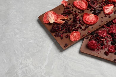 Photo of Chocolate bars with freeze dried berries on grey marble table, closeup. Space for text