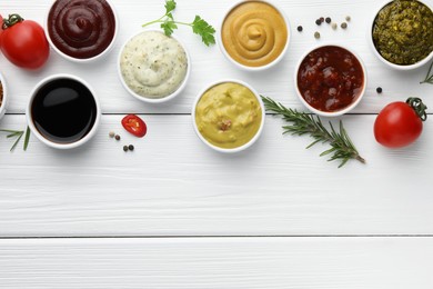 Many different sauces, spices and vegetables on white wooden table, flat lay. Space for text