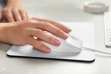 Photo of Woman using wired computer mouse on pad at light grey marble table, closeup