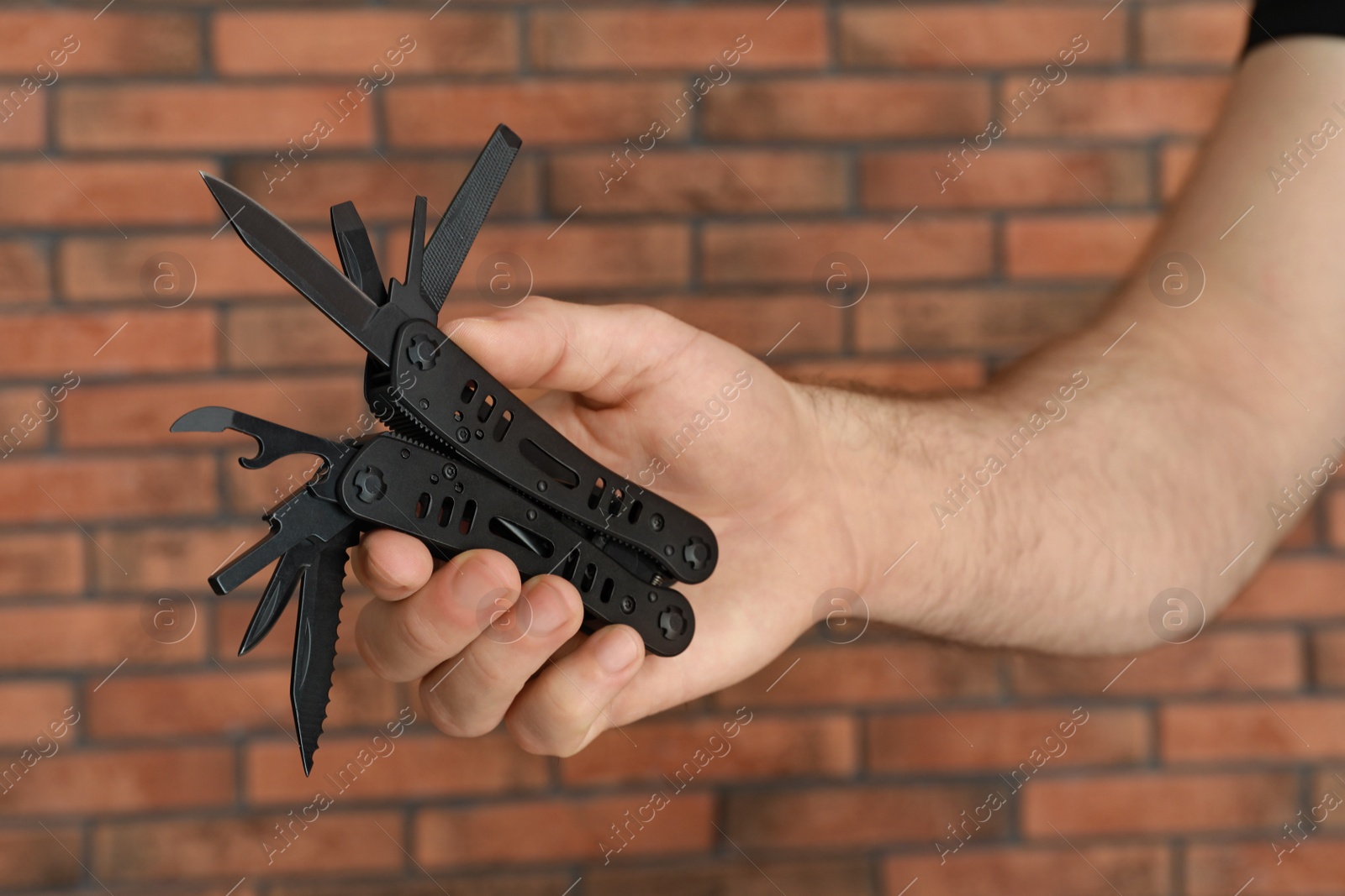 Photo of Man holding multitool near brick wall, closeup