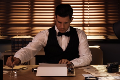 Photo of Old fashioned detective working with typewriter at table in office
