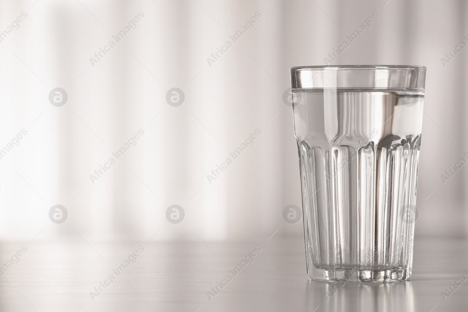 Photo of Glass with water on table against blurred background. Space for text