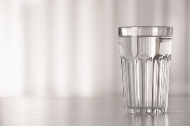 Photo of Glass with water on table against blurred background. Space for text