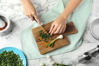 Photo of Woman cutting fresh green onion on table, top view