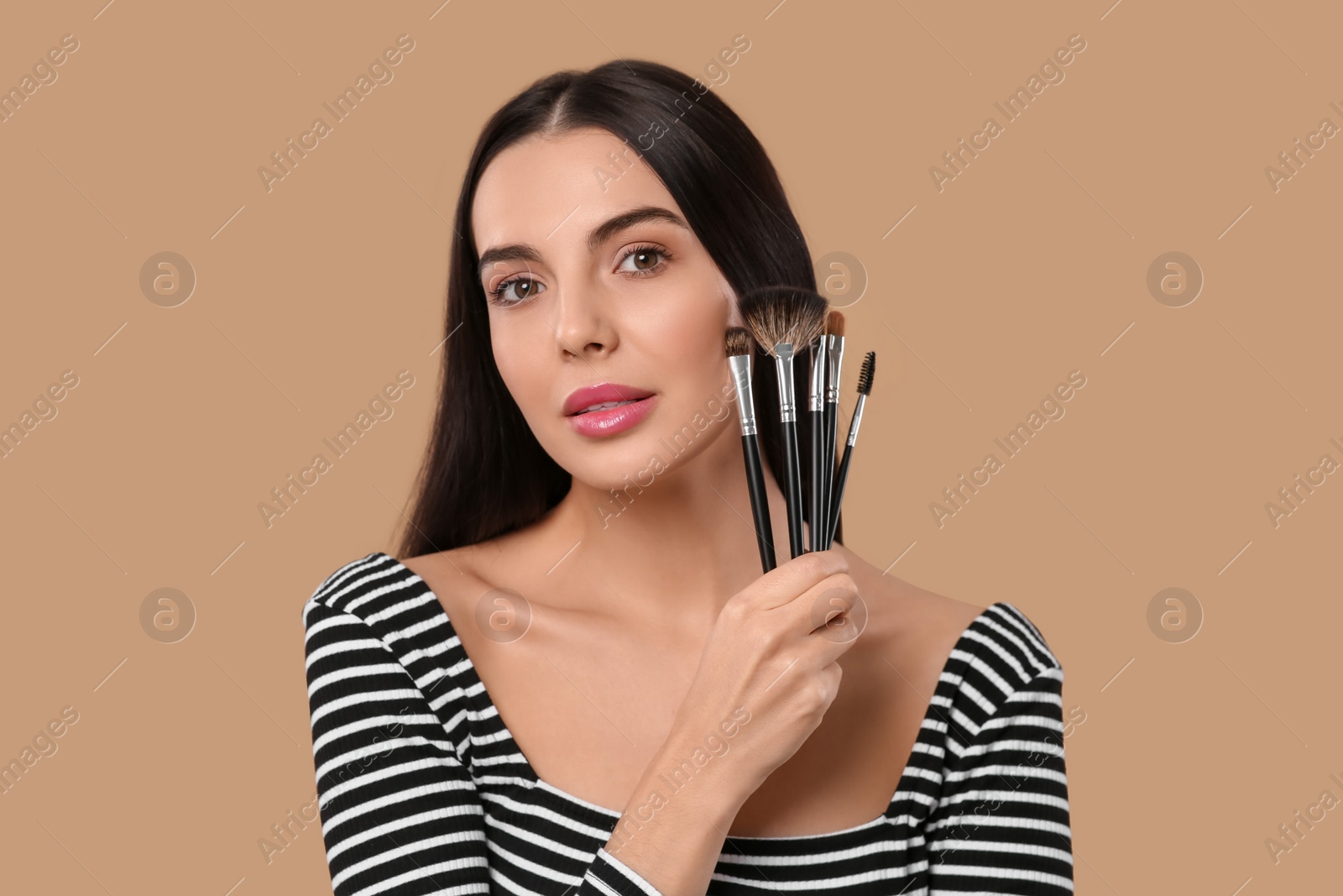 Photo of Beautiful woman with different makeup brushes on light brown background