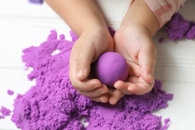 Photo of Little child playing with kinetic sand at white table, closeup