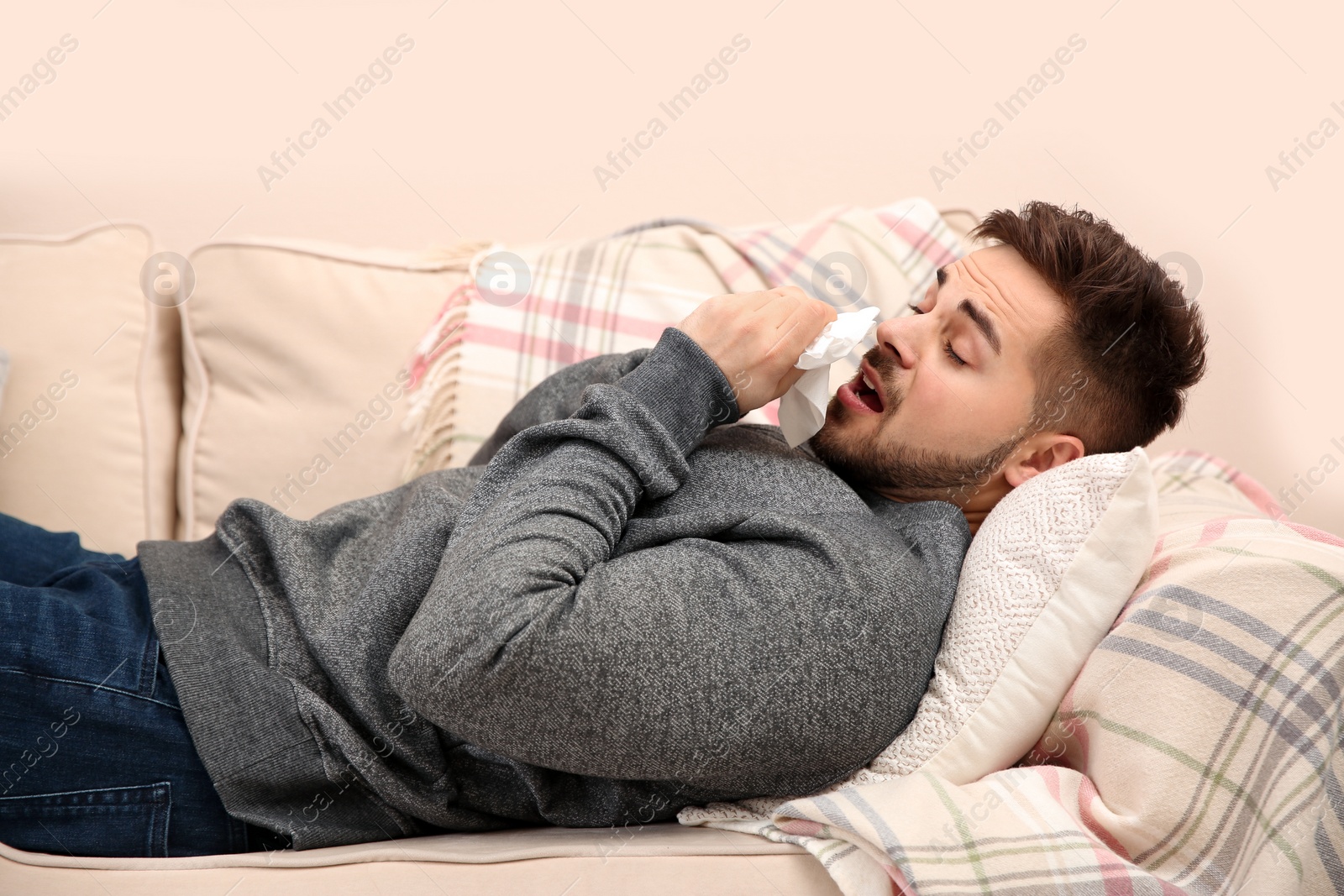 Photo of Sick young man sneezing at home. Influenza virus