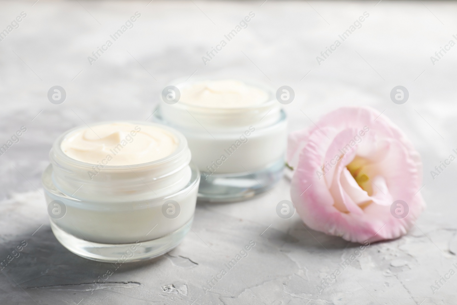 Photo of Closeup view of hand cream jars with flower on gray background