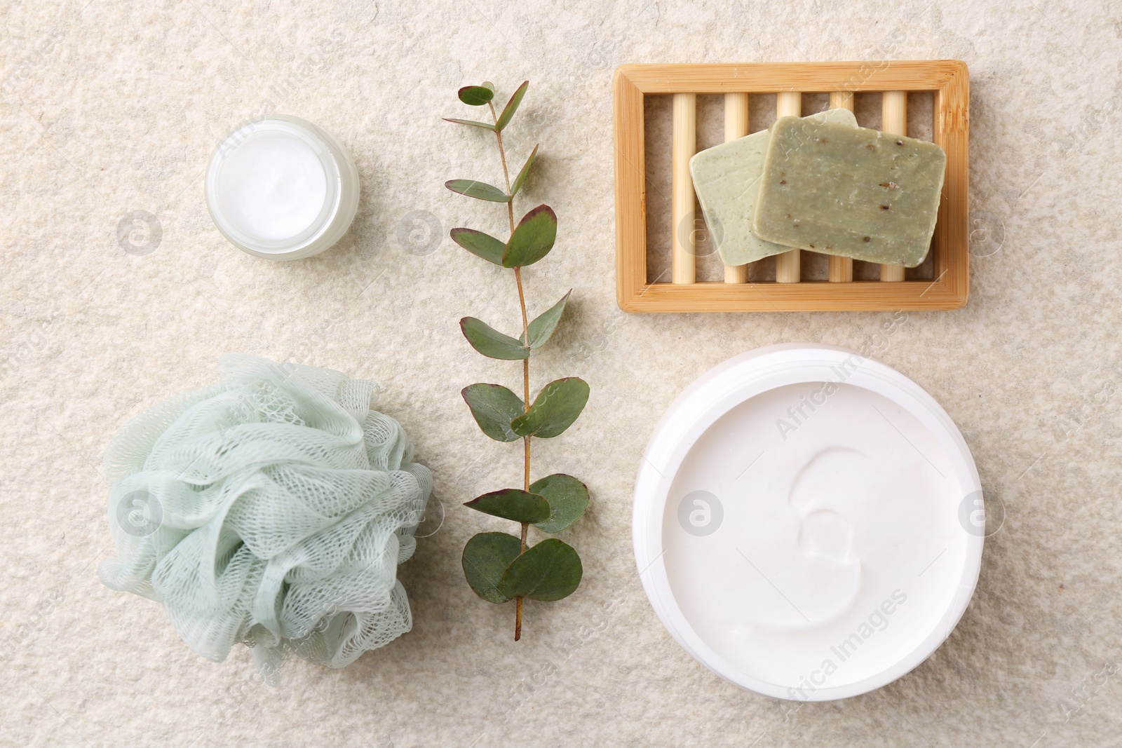 Photo of Flat lay composition with moisturizing cream in open jar and other body care products on light textured table