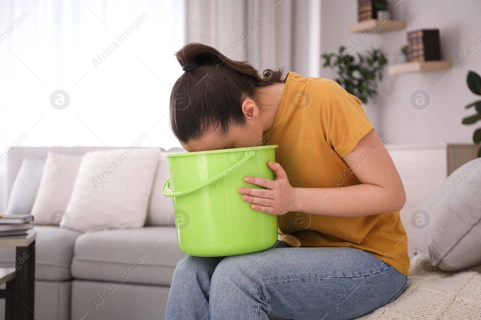 Photo of Young woman with bucket suffering from nausea at home. Food poisoning