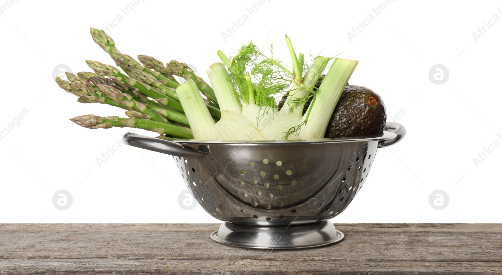 Photo of Metal colander with asparagus, fennel and avocados on wooden table against white background