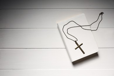 Photo of Cross with chain and Bible on white wooden table, top view with space for text. Religion of Christianity