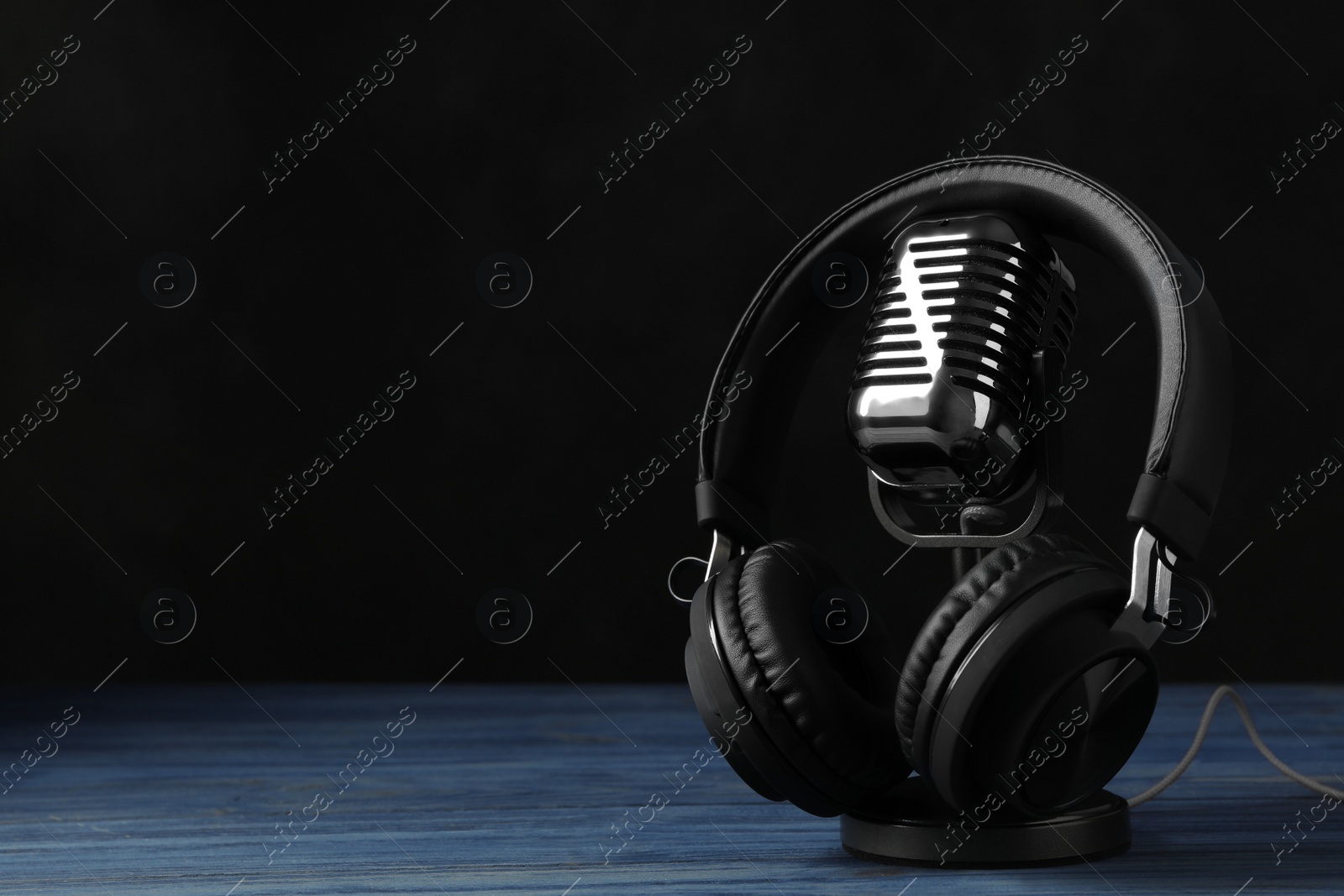 Photo of Retro microphone and headphones on table against dark background. Space for text