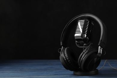 Photo of Retro microphone and headphones on table against dark background. Space for text