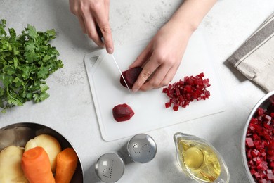 Photo of Woman cutting boiled beetroot at white table, top view. Cooking vinaigrette salad
