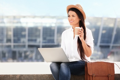 Photo of Beautiful woman with laptop and cup of coffee sitting on stairs outdoors
