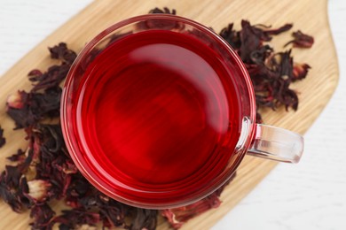 Photo of Cup of fresh hibiscus tea and dry flower leaves on wooden table, flat lay