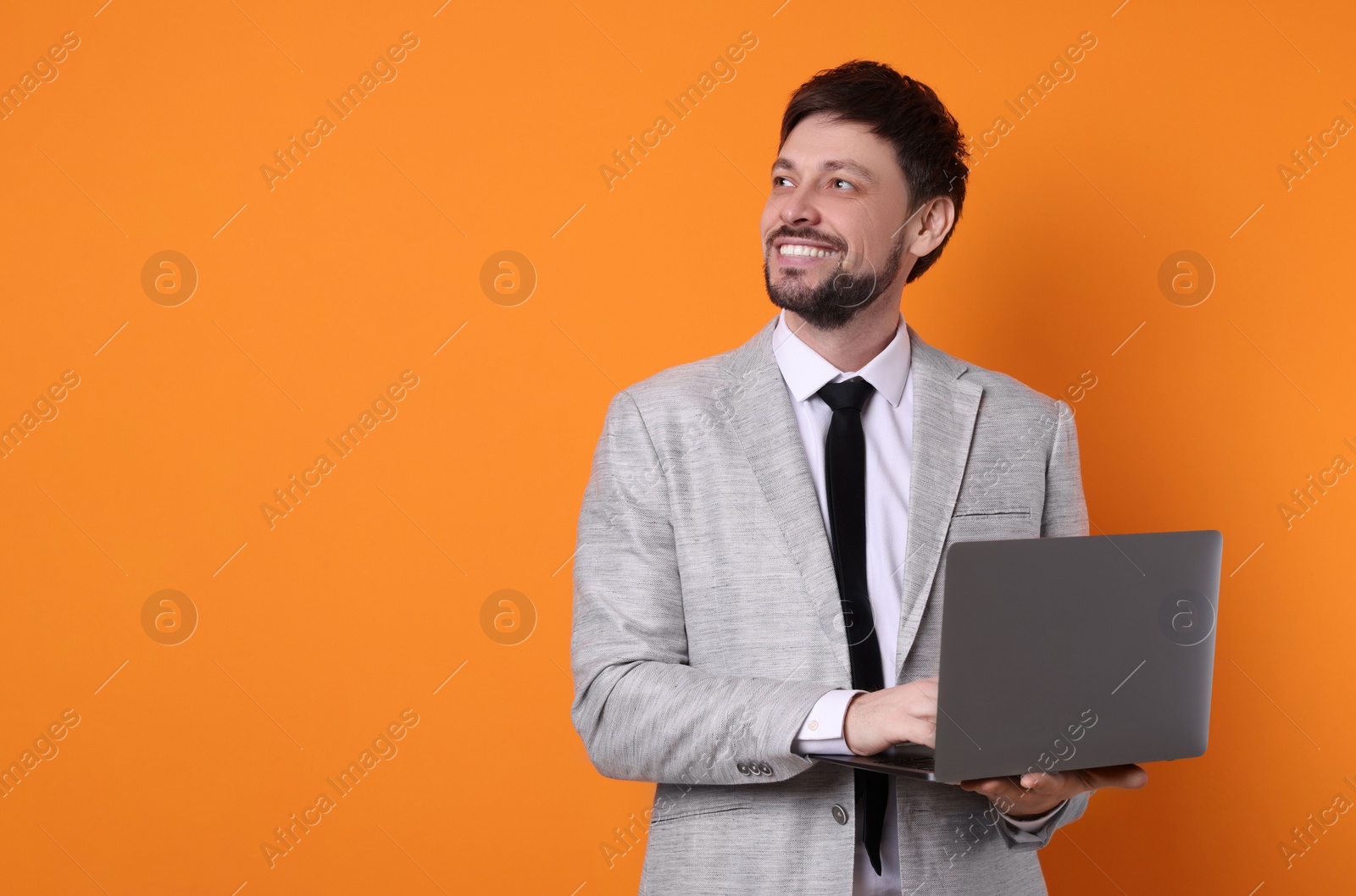 Photo of Happy man with laptop on orange background, space for text