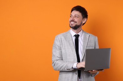 Photo of Happy man with laptop on orange background, space for text