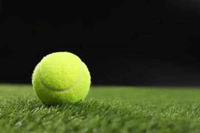 Photo of Tennis ball on green grass against black background, space for text