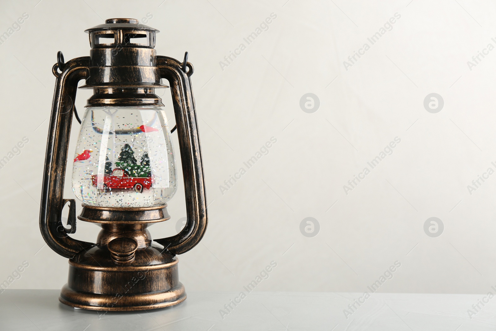 Photo of Beautiful snow globe in vintage lantern on grey table against light background, space for text