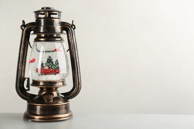 Beautiful snow globe in vintage lantern on grey table against light background, space for text