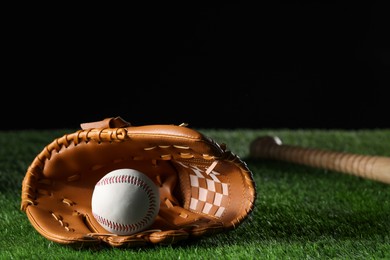 Photo of Baseball glove and ball on artificial grass against black background. Space for text