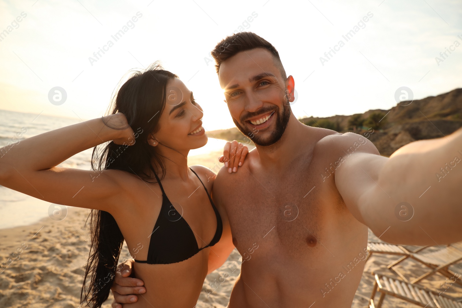 Photo of Happy young couple taking selfie on beach at sunset