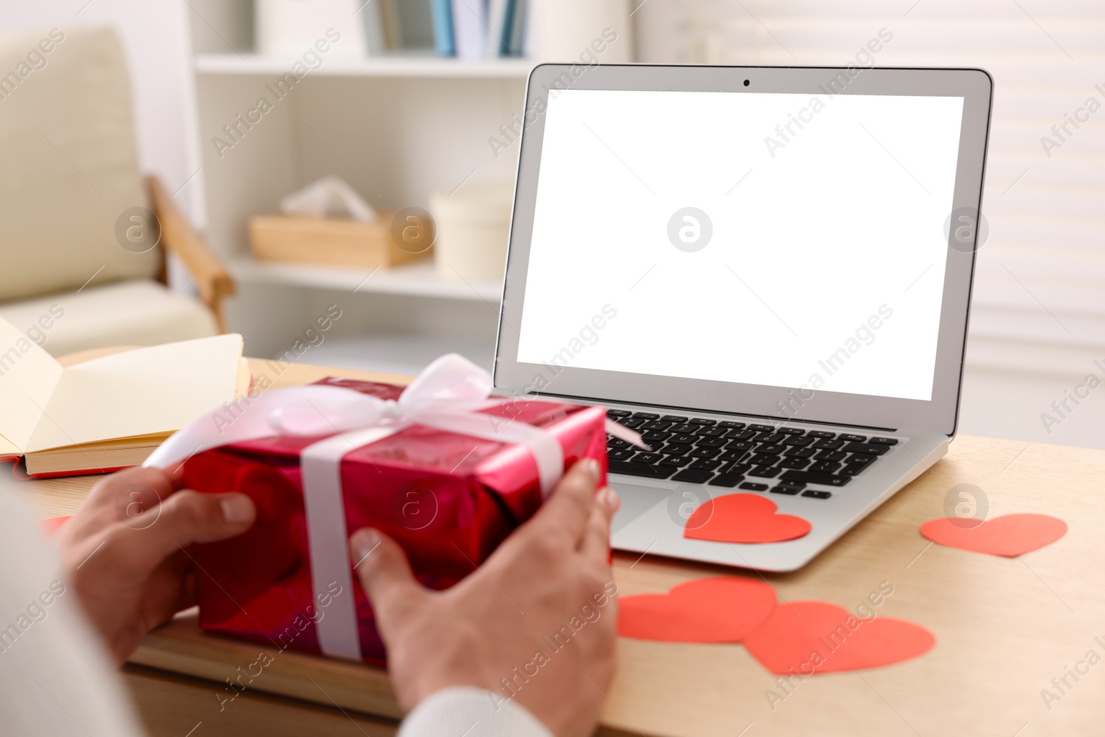 Photo of Valentine's day celebration in long distance relationship. Man holding gift box while having video chat with his girlfriend via laptop, closeup