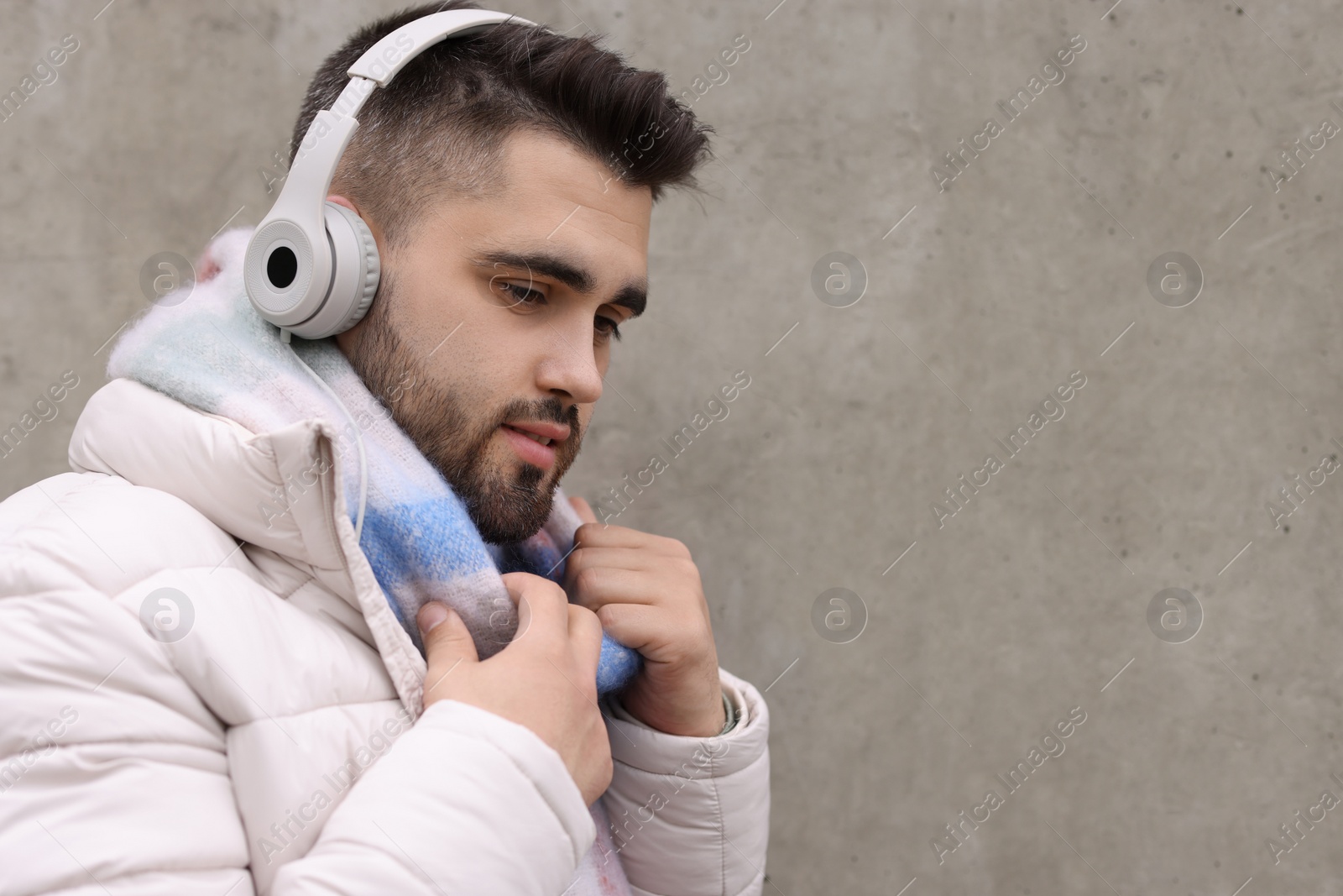 Photo of Handsome man in warm scarf and headphones near wall outdoors. Space for text