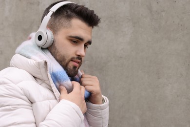 Handsome man in warm scarf and headphones near wall outdoors. Space for text