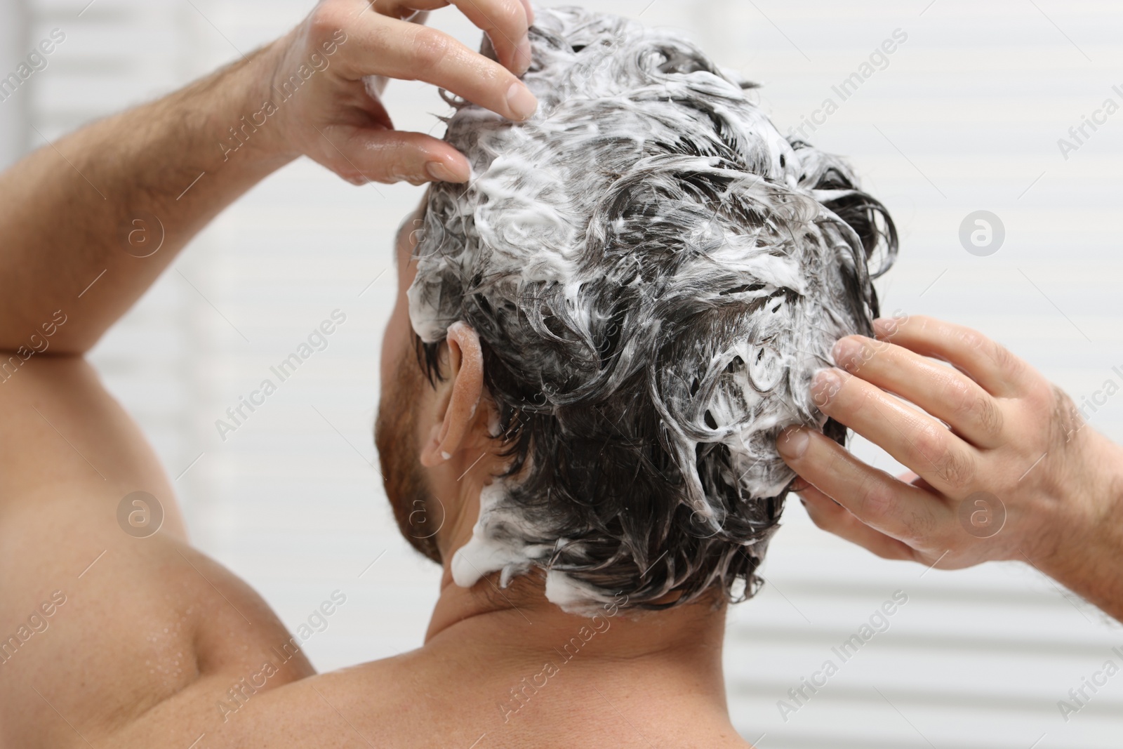 Photo of Man washing his hair with shampoo in shower, back view