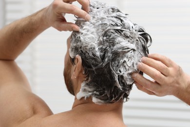 Man washing his hair with shampoo in shower, back view