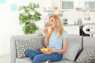 Young woman with bowl of chips watching TV on sofa at home