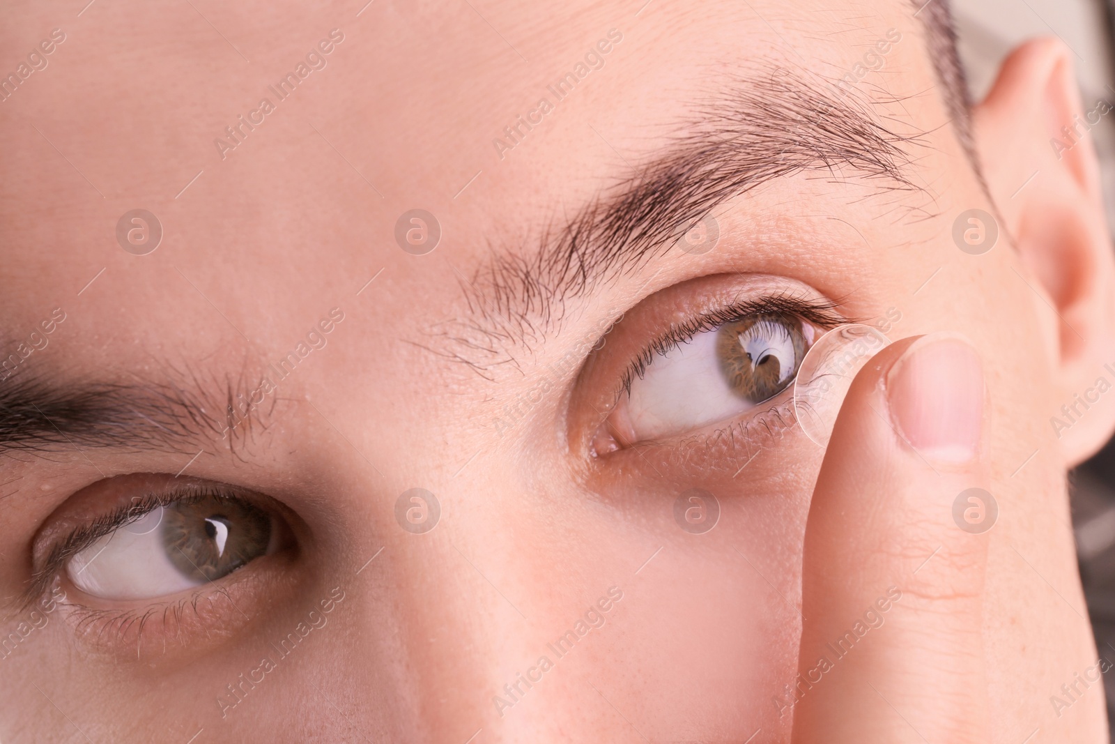 Photo of Young man putting contact lens in his eye, closeup