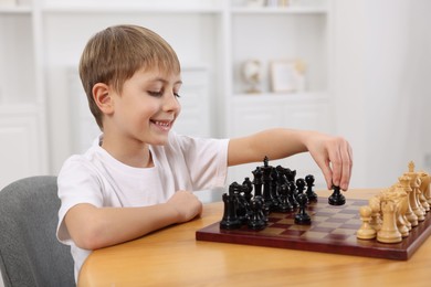 Photo of Cute little boy playing chess at table in room