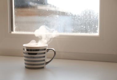 Cup of hot drink near window on rainy day. Space for text