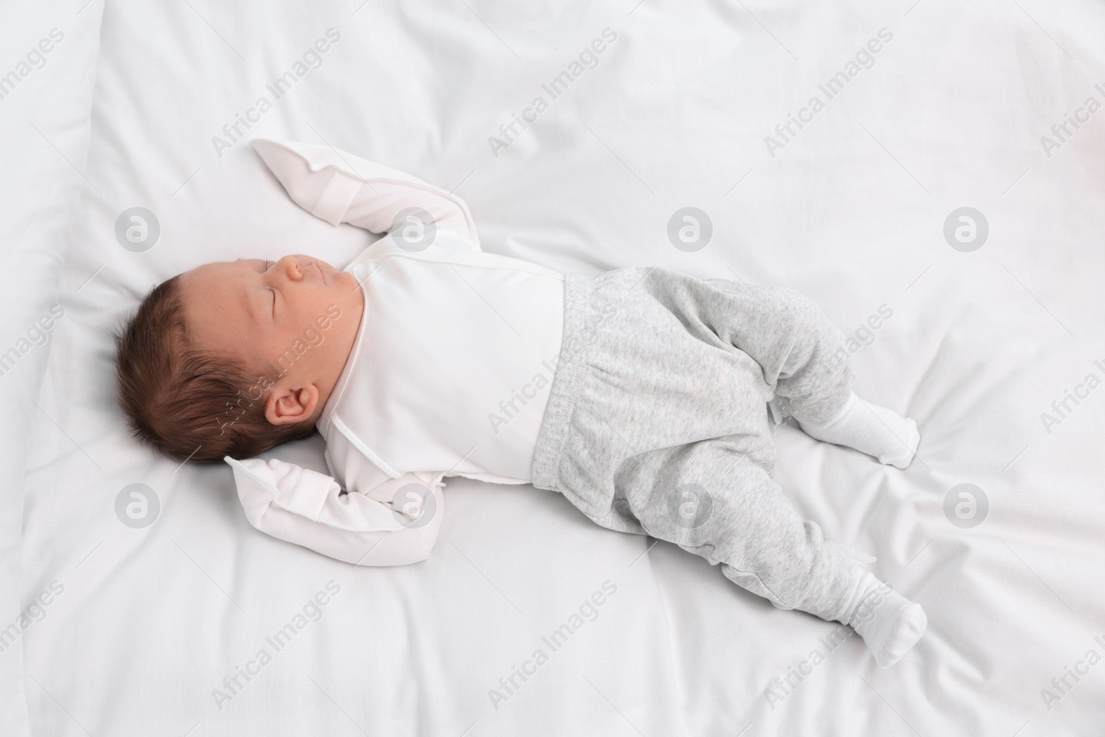 Photo of Cute newborn baby sleeping on white soft bed, top view