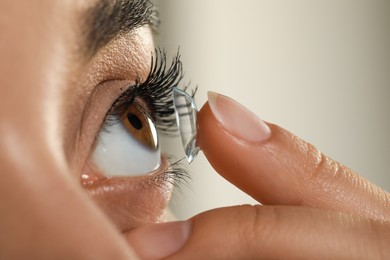 Photo of Young woman putting contact lens in her eye on grey background, closeup