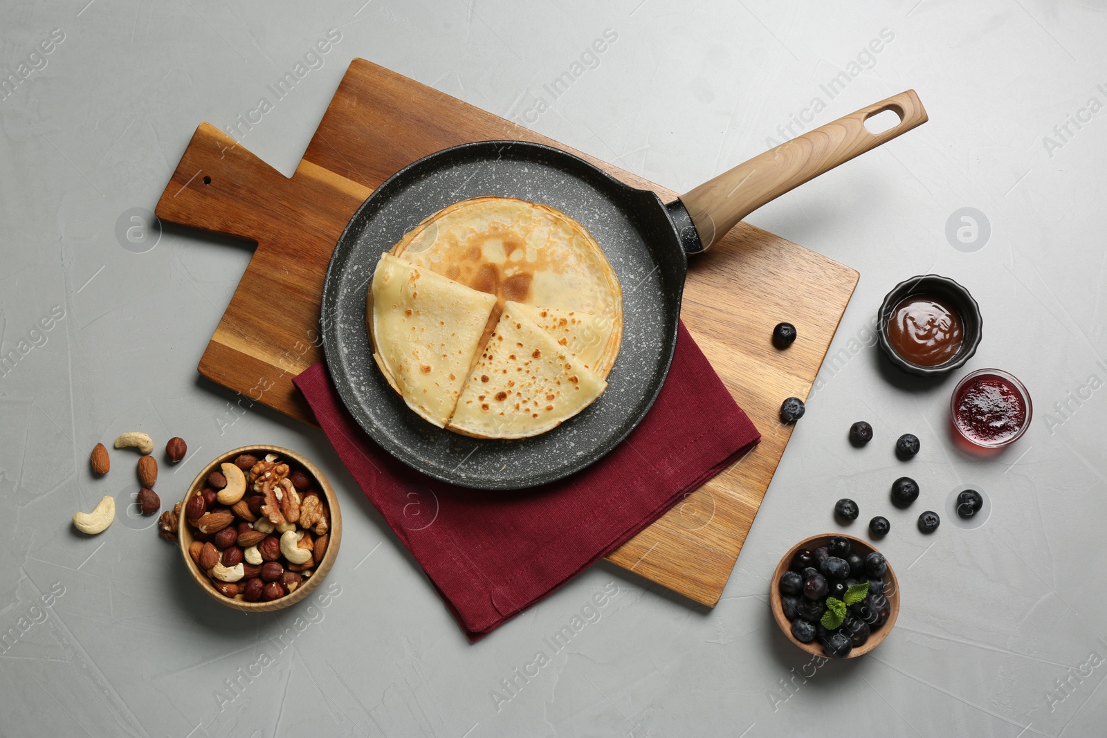 Photo of Delicious crepes with blueberries, mint, nuts and jam on light grey table, flat lay