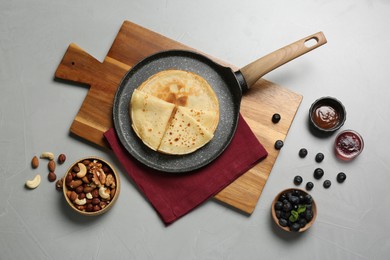 Delicious crepes with blueberries, mint, nuts and jam on light grey table, flat lay